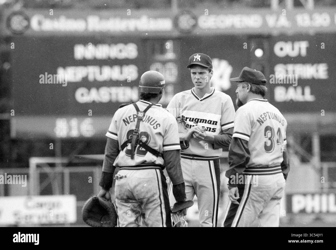 Verschiedenes Nicols Champion, Baseball Haarlem Nicols, 27-08-1989 Whizgle News, Dutch Desk, Niederlande, 1950-2000 drei Baseballspieler diskutieren über die Strategie auf dem Spielfeld und tragen Trikots mit „Neptunus“. Eine Anzeigetafel im Hintergrund zeigt den aktuellen Spielstatus an, einschließlich Innings und Zählungen. Die Szene fängt einen Moment der Konzentration und Teamarbeit während eines Spiels ein. Stockfoto