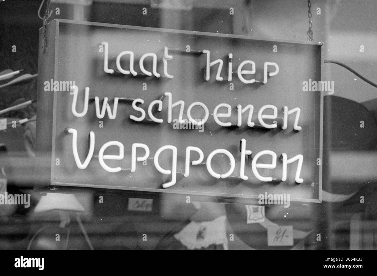 Serie von Crazy Plates repflanzte Schuhe, Platten, 12-08-1987 Whizgle News, Dutch Desk, Niederlande, 1950-2000 Ein leuchtendes Schild in einem Schaufenster zeigt den Text „laat hier uw schoenen vergoten“, der Kunden einlädt, bei schuhbezogenen Dienstleistungen vorbeizuschauen. Stockfoto