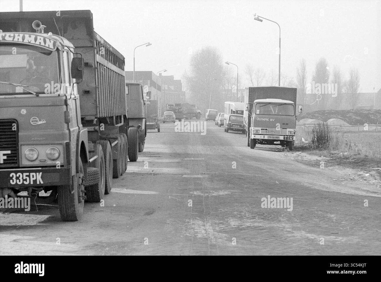 Hendrik Figeeweg mit Wagen entlang der Straße, Straßen, Straßenbau, Straßenbau, Haarlem, Hendrik Figeeweg, Niederlande, 05-12-1978 Whizgle News, Dutch Desk, Niederlande, 1950-2000 Eine Reihe von Lkw, die entlang einer nebeligen, ruhigen Straße geparkt werden, mit Bäumen und Gebäuden, die im Hintergrund leicht sichtbar sind, schafft ein Gefühl industrieller Einsamkeit. Stockfoto