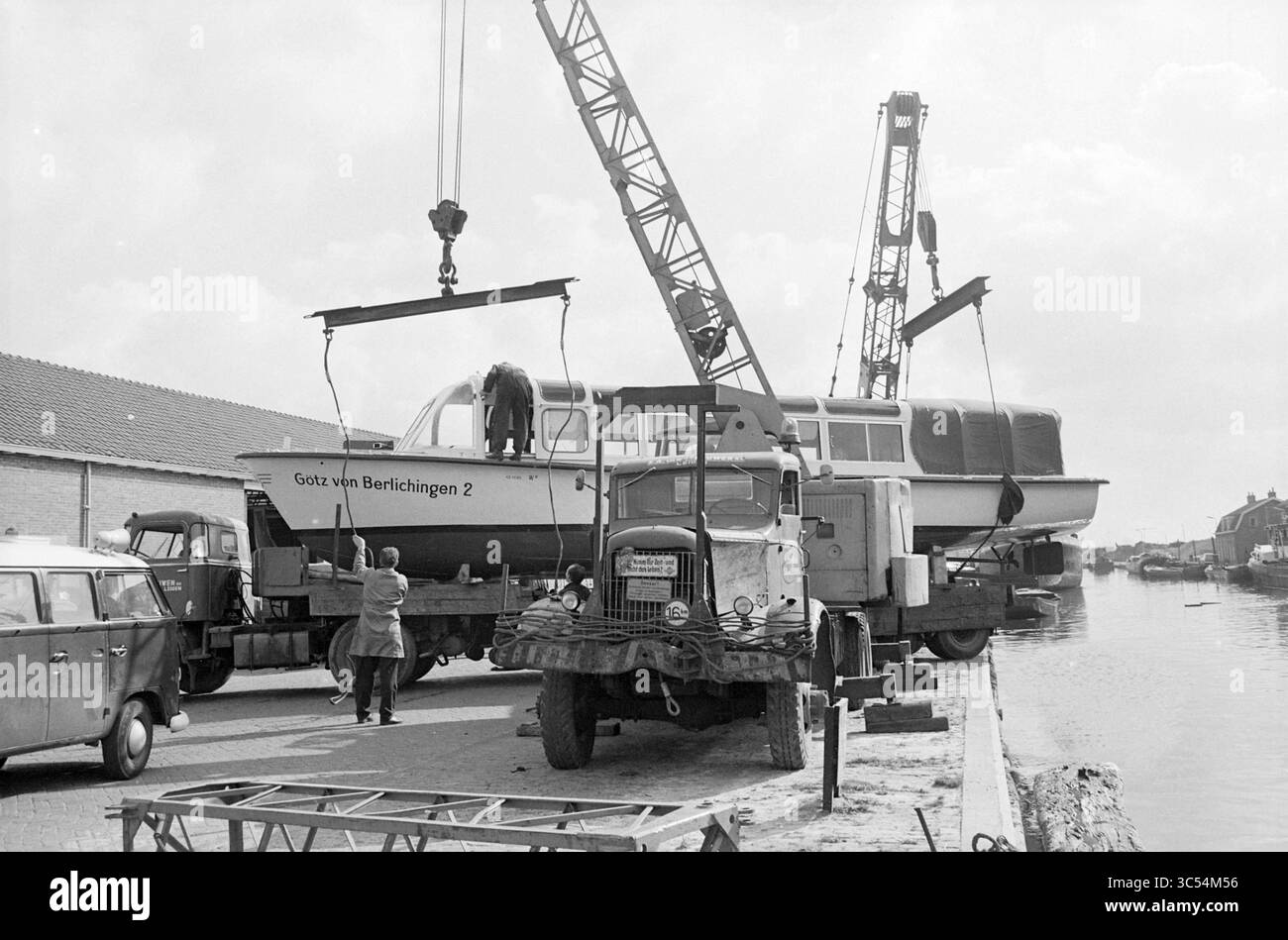 Das Ausflugsboot Götz von Berlichingen 2 mit Heimathafen Titisee wird für den Transport auf einen Lastwagen von S.A. angehoben. Van Leeuwen aus Leiden. Whizgle News, Dutch Desk, Niederlande, 1950-2000 Ein Boot mit dem Namen „Götz von Berlichingen 2“ wird an einer Anlegestelle von Kränen aus dem Wasser gehoben, wobei die Arbeiter aktiv an dem Prozess beteiligt sind. Oldtimer stehen in der Nähe, was zu maritimen Aktivitäten und Industriearbeiten beiträgt. Stockfoto