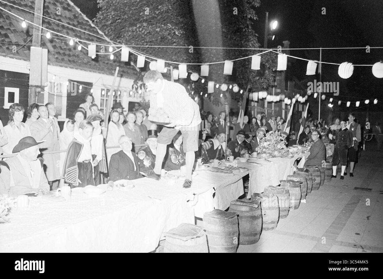Wir feiern das Jahrhundert von Frans Hals. Festliches Milizessen im Stil des 17. Jahrhunderts im Kloveniersdoelen, Haarlem, Niederlande, 28-07-1962 Whizgle News, Dutch Desk, Niederlande, 1950-2000 Ein lebhaftes Treffen im Freien bietet einen langen Tisch voller Speisen, umgeben von einer vielfältigen Menschenmenge, die unter festlicher Dekoration feiert. Ein Darsteller steht auf dem Tisch und unterhält das Publikum, während andere die Festlichkeiten genießen und eine lebendige Atmosphäre der Kameradschaft und Freude schaffen. Stockfoto