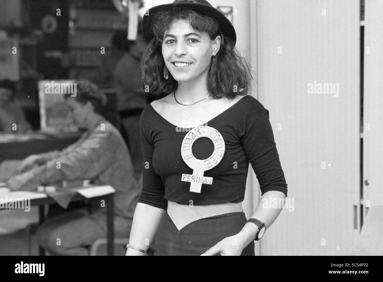 Verschiedene Aktivitäten im Egelantier, darunter Bauchtanz und Chorgesang, im Zusammenhang mit Frauentag, 07-03-1992 Whizgle News, Dutch Desk, Niederlande, 1950-2000 Eine junge Frau mit stilvollem Hut und passendem Top mit verspieltem Design lächelt selbstbewusst und verkörpert eine Mischung aus Kreativität und Persönlichkeit. Sie trägt ein Abzeichen, das ihr Engagement bei einem lebendigen Community-Event vor dem Hintergrund von Menschen und Aktivitäten unterstreicht. Stockfoto