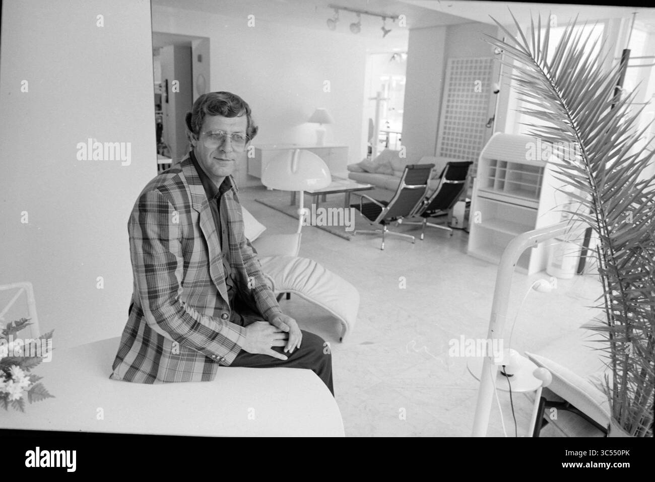 Porträt eines Mannes in einer Inneneinrichtung, 00-10-1984 Whizgle News, Dutch Desk, Niederlande, 1950-2000 Ein Mann in einem karierten Blazer sitzt lässig auf einem modernen Möbelstück, umgeben von einem stilvollen Interieur mit eleganten Möbeln und minimalistischer Einrichtung. Die Atmosphäre vermittelt ein Gefühl von zeitgenössischer Eleganz. Stockfoto