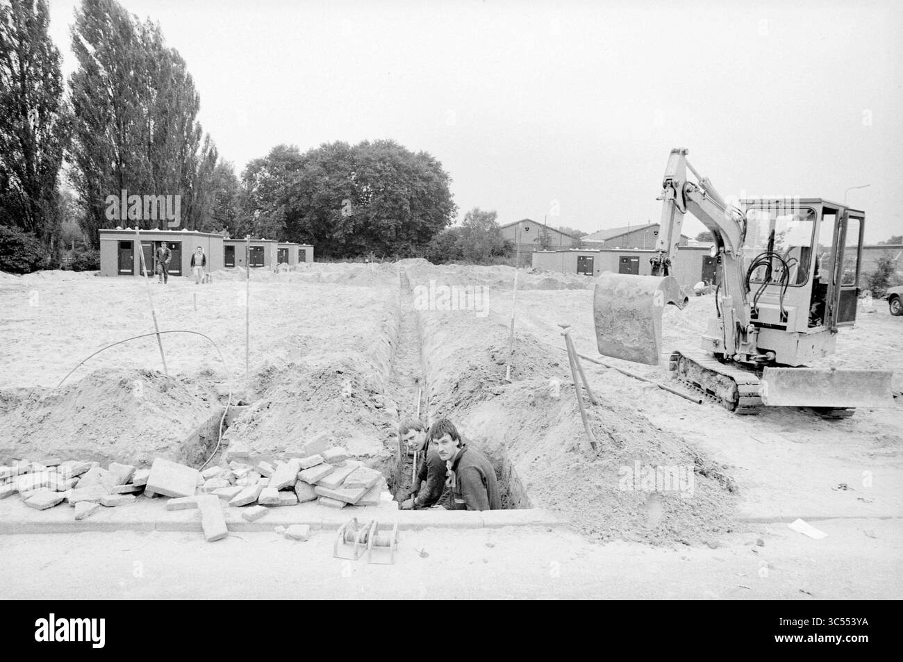 Weerlaan, Hillegom, Straßenbau, Straßen, Straßenbau, Road Planting, Hillegom, Weerlaan, 22-09-1986 Whizgle News, Dutch Desk, Niederlande, 1950-2000 Eine Baustelle mit zwei Arbeitern in einem Graben, mit Erdbewegungsmaschinen in der Nähe und provisorischen Bauwerken im Hintergrund. Bäume säumen das Gebiet und zeigen die Anfangsphasen eines Entwicklungsprojekts an. Stockfoto