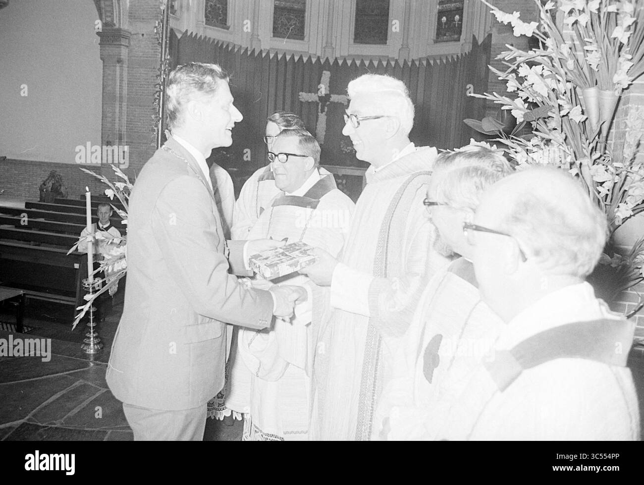 Messe in einer Kirche und Präsentation des Geschenks, 03-09-1972 Whizgle News, Dutch Desk, Niederlande, 1950-2000 Eine Gruppe von Männern, die in zeremoniellen Gewändern gekleidet sind, versammelt sich in einer kirchlichen Umgebung. Ein Mann, lächelnd und in einem Anzug, überreicht einem anderen Mann, der anscheinend ein Klerusmitglied ist, ein Geschenk. Die Szene spiegelt einen Moment der Feier oder Anerkennung wider, mit religiösen Symbolen, die im Hintergrund leicht sichtbar sind. Stockfoto