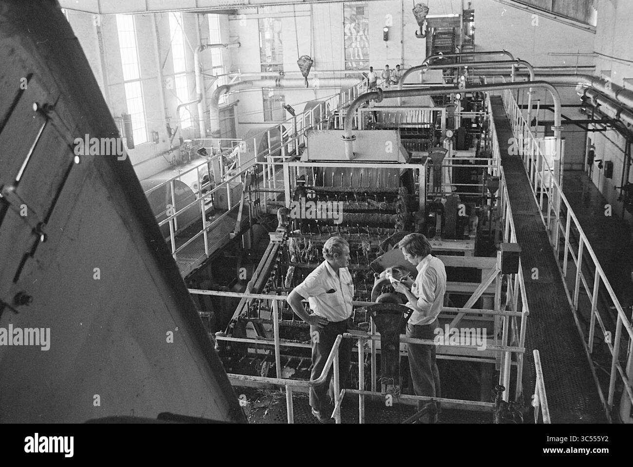 Bericht von Poppe de Boer über Äthiopien, Äthiopien, Bericht, Ethiopië, 00-02-1971 Whizgle News, Dutch Desk, Niederlande, 1950-2000 zwei Personen diskutieren in einem großen industriellen Umfeld, umgeben von Maschinen und Geräten. Der Raum ist mit Rohren und mechanischen Komponenten gefüllt, die eine geschäftige und funktionale Umgebung widerspiegeln, die typisch für eine Industrieanlage ist. Stockfoto