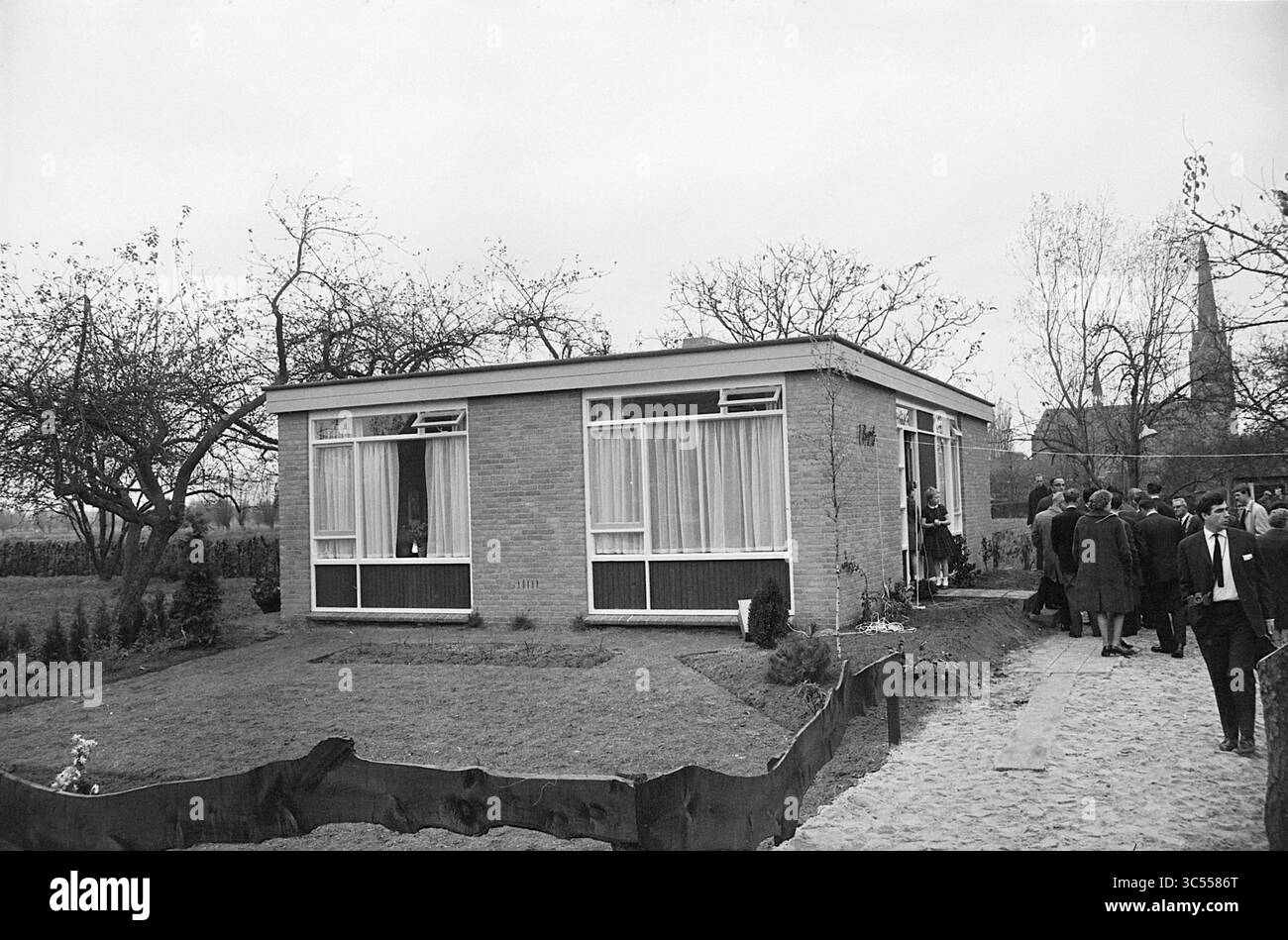 1. Bogaars House in Dinther N.B., Außenansicht, Häuser und Hausbau, Innenraum, 07-11-1963 Whizgle News, Dutch Desk, Niederlande, 1950-2000 Ein bescheidenes, modernistisches Haus mit großen Fenstern, umgeben von einem gepflegten Rasen und Bäumen. Eine Gruppe von Personen in formeller Kleidung steht in der Nähe, die scheinbar in Gesprächen oder Beobachtungen involviert sind, während die Atmosphäre auf ein bedeutendes Ereignis oder Treffen hindeutet. Stockfoto