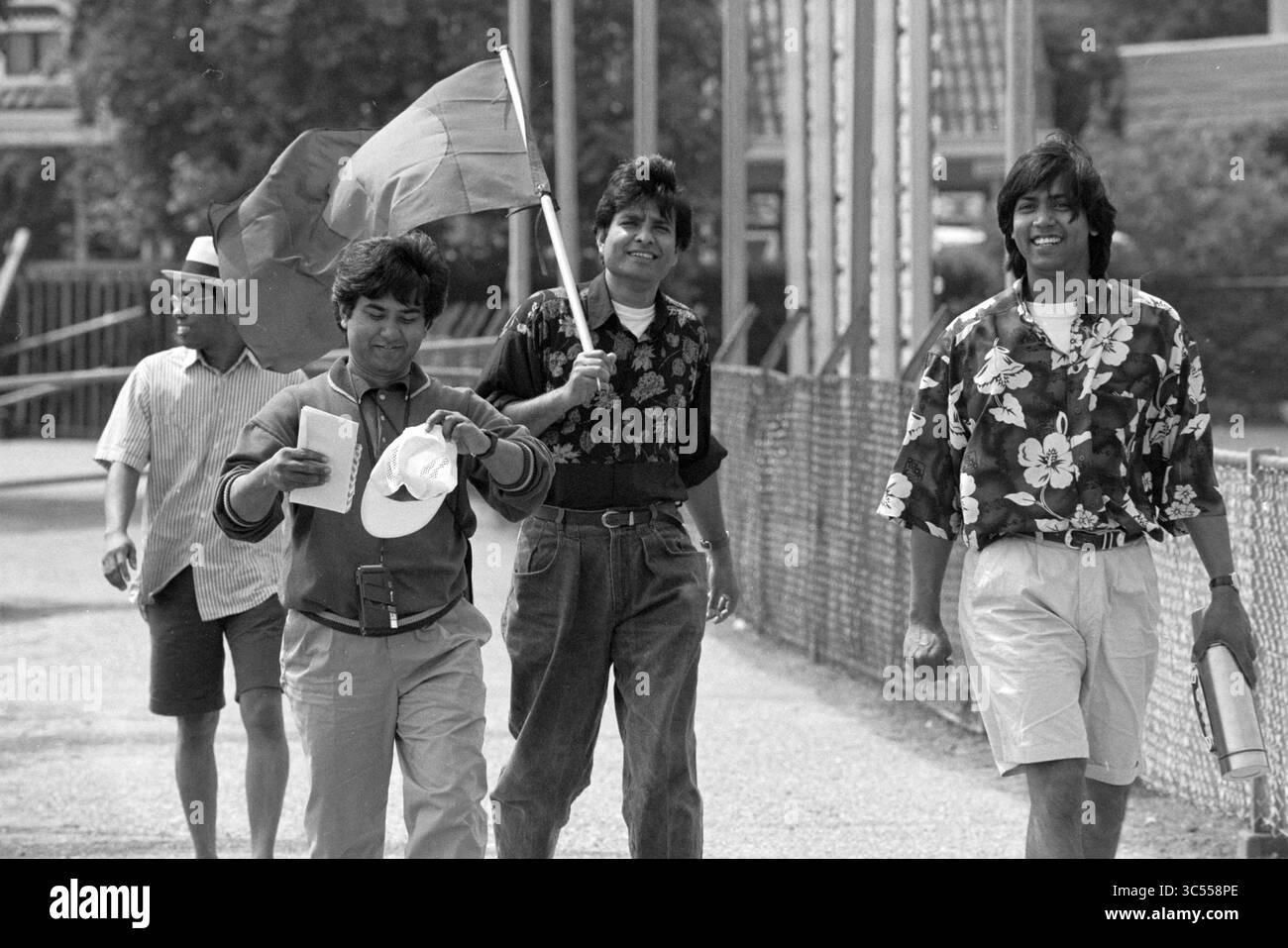 Atmosphere Cricket Canada - Bangladesch, 18-06-1990 Whizgle News, Dutch Desk, Niederlande, 1950-2000 Eine Gruppe von vier Männern spaziert gemeinsam auf einem Weg und präsentiert farbenfrohe Blumenhemden. Ein Mann trägt stolz eine Flagge, während ein anderer ein Blatt Papier hält. Sie wirken entspannt und gemütlich und genießen die Gesellschaft und den Tag. Stockfoto