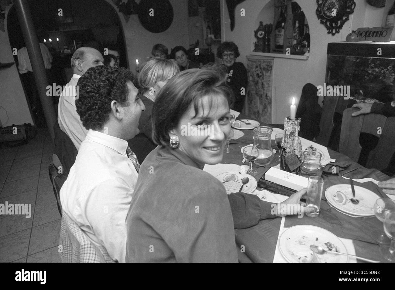 Wedding Pizza @@ronno, H'lem [Saronno], Haarlem, Niederlande, 05-11-1992 Whizgle News, Dutch Desk, Niederlande, 1950-2000 Ein lebhaftes Treffen an einem Esstisch, bei dem Gäste sich unterhalten und ihre Mahlzeiten genießen. Eine Frau im Vordergrund lächelt in die Kamera, während andere im Hintergrund Lachen und Kameradschaft teilen, beleuchtet von sanftem Kerzenlicht. Stockfoto