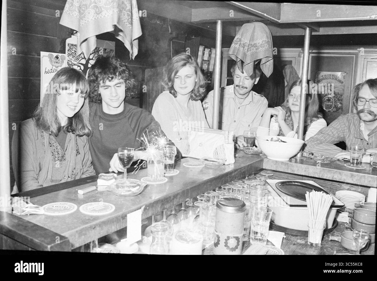 Silvester 1979-1980, fünf junge Leute in einer Bar mit Sparklern, 31-12-1979, Whizgle News, Dutch Desk, Niederlande, 1950-2000 Eine lebhafte Bar-Szene mit einer Gruppe von Freunden, die Drinks und Gespräche genießen, wobei eine Person einen Cocktail mischt. Die Atmosphäre ist warm und entspannt und unterstreicht Kameradschaft und Spaß. Stockfoto