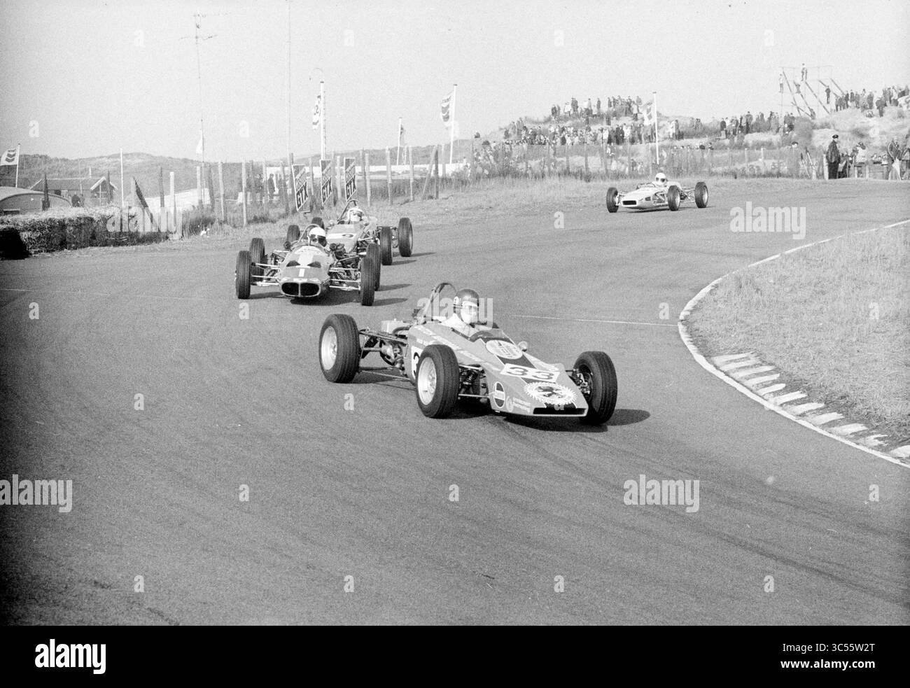 Autorennen für die Zandvoort Trophy 1970, Zandvoort, 30 2011-08-1970 Whizgle News, Dutch Desk, Niederlande, 1950-2000 Eine Gruppe von Oldtimer fährt auf einer kurvenreichen Strecke, wobei ein Fahrer die Führung übernimmt und die Spannung des Motorsports demonstriert. Die Zuschauer beobachten von der Seitenlinie aus, wie die Fahrzeuge vorbeifahren und betonen den Nervenkitzel des Wettkampfsports. Stockfoto
