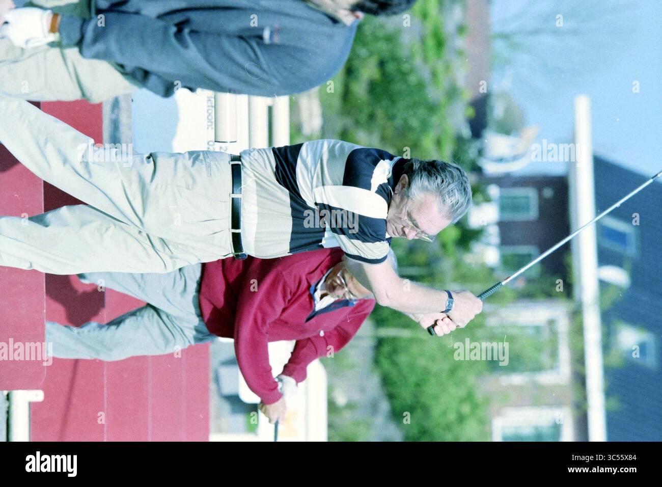 Herr van der Wind, Golfplatz Vijfhuizen, Vijfhuizen, 26-04-1999 Whizgle News, Dutch Desk, Niederlande, 1950-2000 Ein Golfspieler schwingt seinen Club mit Fokus auf einen üppigen grünen Golfplatz, während zwei andere Personen von hinten beobachten, die am Spiel beteiligt sind. Stockfoto