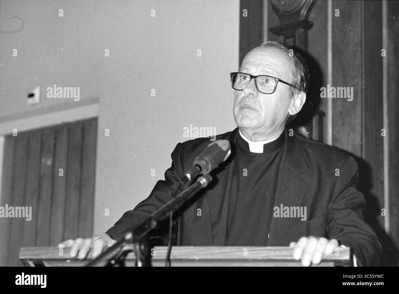 J. Steinkamp, Redner, 18-01-1993 Whizgle News, Dutch Desk, Niederlande, 1950-2000 Ein Klerus steht auf einem Podium und spricht mit ernstem Ausdruck. Er trägt eine Brille und ein traditionelles klerikales Outfit, das ein Gefühl von Autorität und Engagement für das Publikum vermittelt. Der Hintergrund ist mit Holzdetails versehen, die der Umgebung einen Hauch Wärme verleihen. Stockfoto