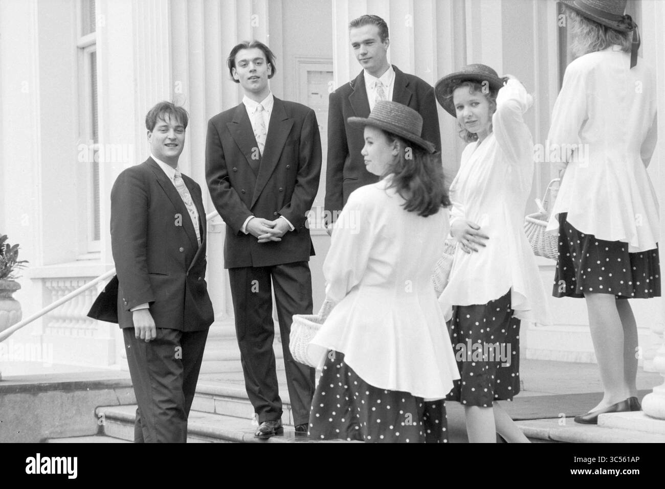 Blumenjungen in BL'daal, Bloemendaal, 18-03-1991 Whizgle News, Dutch Desk, Niederlande, 1950-2000 Eine Gruppe elegant gekleideter Individuen steht auf einer Treppe, die sich unterhalten und lachen. Einige tragen stilvolle Hüte, andere tragen Blumenmuster auf ihrer Kleidung, was eine charmante, soziale Atmosphäre schafft. Im Hintergrund befindet sich ein elegantes Gebäude, das das Gefühl der Raffinesse noch verstärkt. Stockfoto