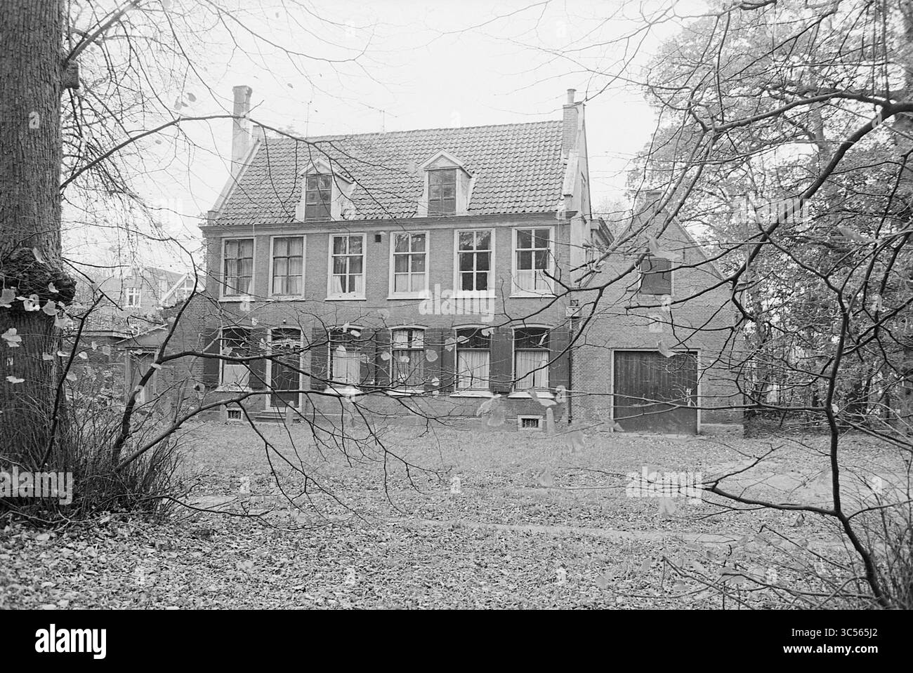 Landsitz Zomerlust, Wagenweg 65, Haarlem, Wagenweg 65, Niederlande, 03-11-1969 Whizgle News, Dutch Desk, Niederlande, 1950-2000 Ein prächtiges Backsteinhaus mit mehreren Fenstern, umgeben von kargen Bäumen, zeigt einen klassischen architektonischen Stil. Der bewachsene Hof ist mit gefallenen Blättern bedeckt, was dem Schauplatz einen Hauch von Verlassenheit verleiht. Stockfoto