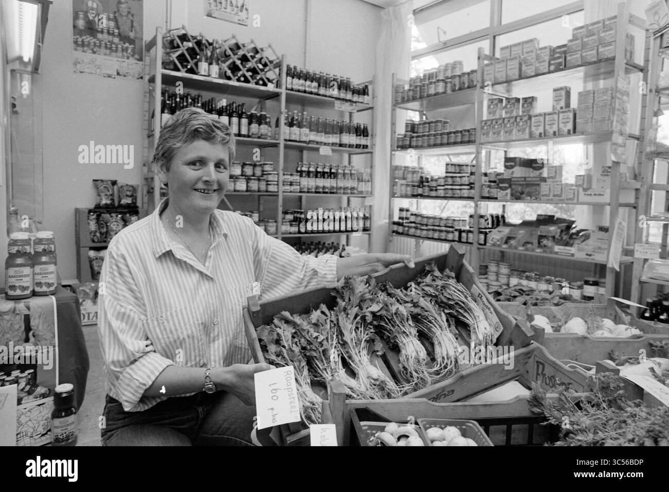 Ria Hogervoorst, Hoofddorp, Niederlande, 28-05-1990 Whizgle News, Dutch Desk, Niederlande, 1950-2000 Ein Händler stellt stolz eine Kiste frischer Kräuter auf einem geschäftigen Markt vor, umgeben von Regalen, die mit verschiedenen verpackten Waren und Flaschen gefüllt sind. Helle Beleuchtung unterstreicht die lebhafte Atmosphäre des Geschäfts. Stockfoto