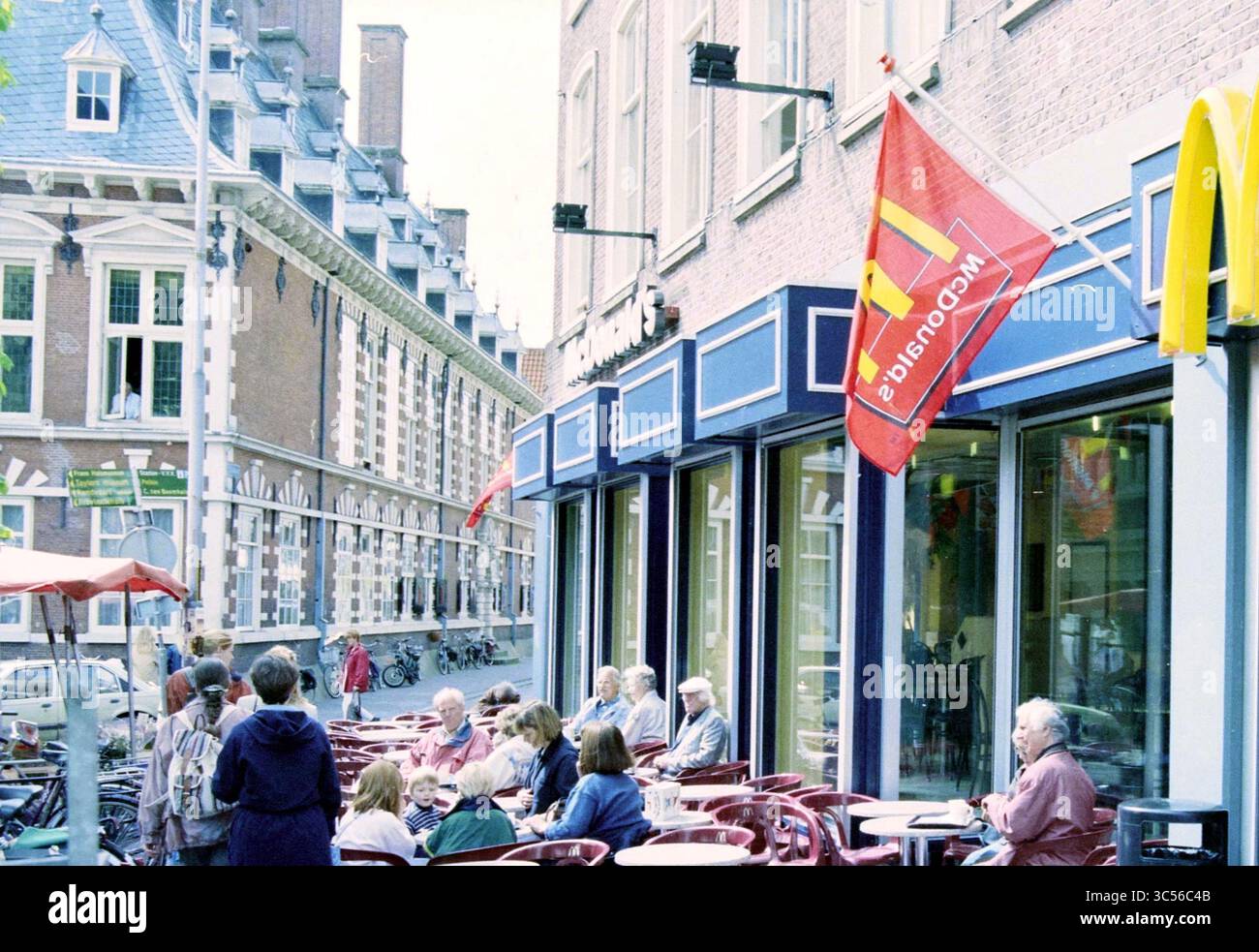 Illegale Terrasse McDonalds Grote Markt, Haarlem, Grote Markt, Niederlande, 25-05-1997 Whizgle News, Dutch Desk, Niederlande, 1950-2000 In Einer lebhaften Straßenszene befindet sich ein McDonald's Restaurant, in dem die Gäste ihre Mahlzeiten an Tischen im Freien genießen können. Farbenfrohe Fahnen flattern darüber, und nahe gelegene Gebäude zeigen klassische Architekturstile. Eine Mischung von Gästen, von Familien bis Individuen, trägt zur lebhaften Atmosphäre des Ortes bei. Stockfoto