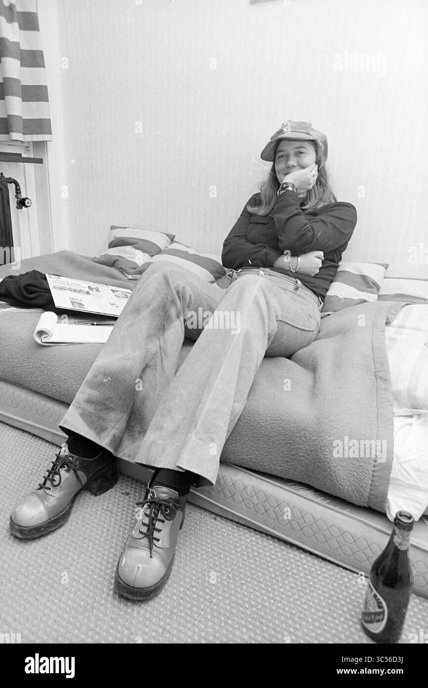 Porträt der jungen Frau, Haarlem, Niederlande, 00-00-1972 Whizgle News, Dutch Desk, Niederlande, 1950-2000 Eine Person liegt auf einem Bett, in einem legeren Outfit mit weiträumigen Hosen und stabilen Stiefeln. Sie tragen eine Mütze und schauen nachdenklich zur Seite, umgeben von einer gemütlichen Schlafzimmeratmosphäre. In der Nähe befindet sich eine Flasche, die die entspannte Atmosphäre der Szene noch verstärkt. Stockfoto