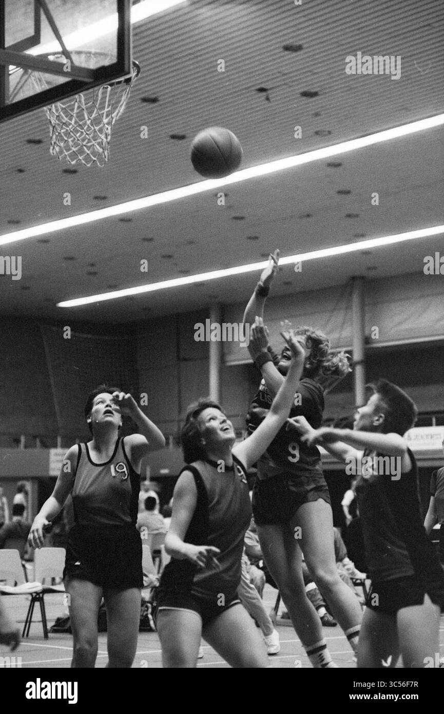 Basketballspiel Whizgle News, Dutch Desk, Niederlande, 1950-2000 Ein dynamischer Moment auf dem Basketballfeld fängt Athleten in Aktion Ein, wobei ein Spieler zum Schießen springt, während andere das Spiel vorwegnehmen. Der Wettkampfgeist ist spürbar, da sich Teamkameraden und Gegner gleichermaßen auf den Ball konzentrieren, der auf den Basketball schwebt. Stockfoto