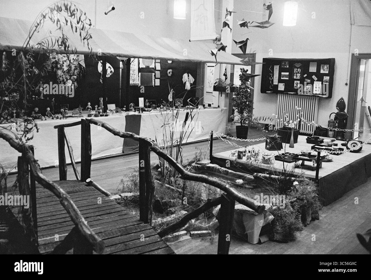Japanische Ausstellung, Jac. P. Thijsse Lyceum, Exhibitions, 05-11-1962 Whizgle News, Dutch Desk, Niederlande, 1950-2000 eine Innenausstellung bietet eine wunderschön angeordnete Ausstellung mit einer Holzbrücke, die zu verschiedenen dekorativen Gegenständen, Pflanzen und künstlerischen Installationen führt. Das Layout umfasst lebendige Dekorationen und visuelle Elemente, die eine einladende Atmosphäre schaffen und kulturelle oder künstlerische Themen präsentieren. Stockfoto