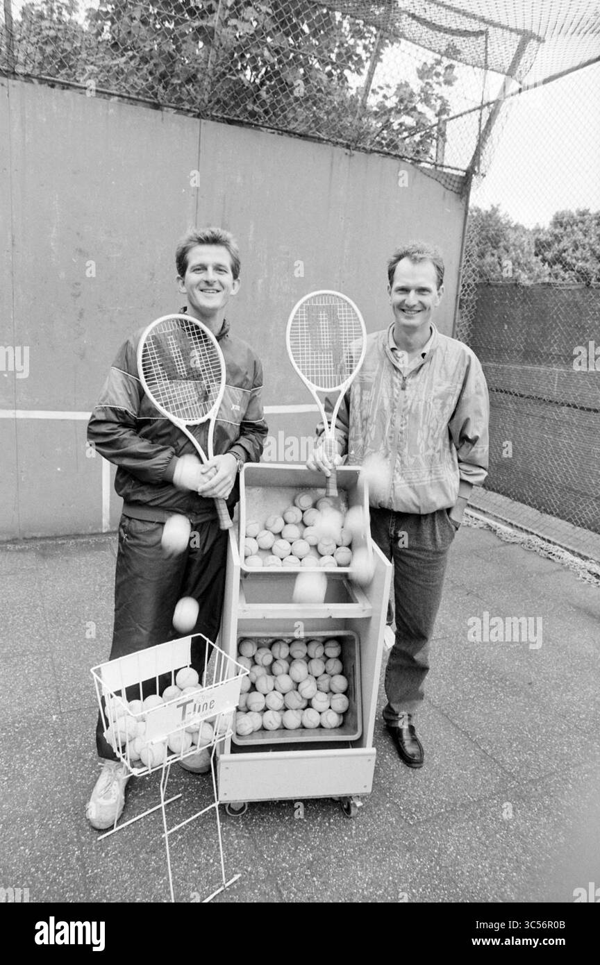 Mr. Zuidam + Bouten Tennisschule Groenendaal, Tennis, 02-08-1989 Whizgle News, Dutch Desk, Niederlande, 1950-2000 zwei lächelnde Personen stehen auf einem Tennisplatz, jeder hält einen Tennisschläger. Vor ihnen befindet sich ein mit Tennisbälle gefüllter Wagen, zusammen mit einem kleinen Korb. Die Kulisse bietet ein Tennisnetz und umliegende Fechten. Stockfoto