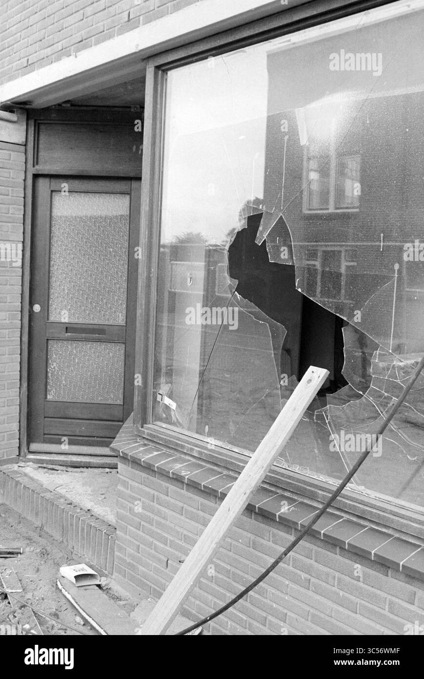 Zerstörte Fenster im Neubau Oud IJmuiden, Neubau, Abbruch, IJmuiden, Niederlande, 02-07-1980 Whizgle News, Dutch Desk, Niederlande, 1950-2000 Ein kaputtes Fenster zeigt eine zerbrochene Reflexion, mit einem großen Loch im Glas, das auf jüngsten Vandalismus hindeutet. Eine Holzdiele liegt über der Szene, die das Gefühl der Verwirrung außerhalb eines bescheidenen Ziegelgebäudes verstärkt. Stockfoto