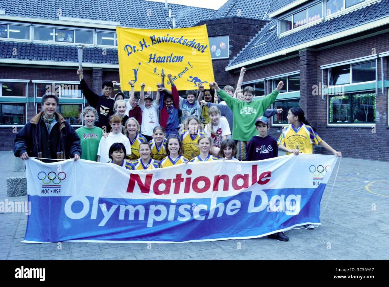 Olympiasieger Yvonne van Gennip (vorne links) im Rahmen des Nationalen Olympischen Tages NOC*NSF in der Dr. H. Bavinckschool, Rechthuisstraat Ecke Ambachtstraat, Haarlem, Rechthuisstraat, Niederlande, 31 03.03.1998 Whizgle News, Dutch Desk, Niederlande, 1950-2000 Eine Gruppe begeisterter Studenten und Erwachsener posiert gemeinsam und feiert mit bunten Bannern eine besondere Veranstaltung, die für „nationale Olympische Dag“ werben. Die Kinder tragen dazu passende Sportuniformen und ihre fröhlichen Ausdrucksformen spiegeln Spannung und Teamarbeit wider. Stockfoto