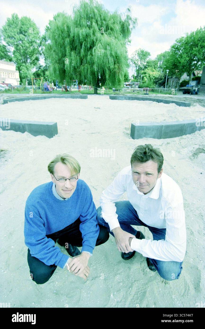 Zwei Mitarbeiter der Gemeinde Haarlem im Park/Spielplatz Godfried van Bouillonstraat, Haarlem, Godfried van Bouillonstraat, Niederlande, 02-09-2003 Whizgle News, Dutch Desk, Niederlande, 1950-2000 zwei Männer hocken sich auf einem sandigen Gebiet, umgeben von einem runden Layout aus dunklen Materialien. Im Hintergrund bietet ein großer Baum Schatten, und einige Gebäude sind am Rand des Raumes sichtbar. Die Szene vermittelt ein Gefühl der Vorfreude auf ein bevorstehendes Projekt oder Ereignis. Stockfoto