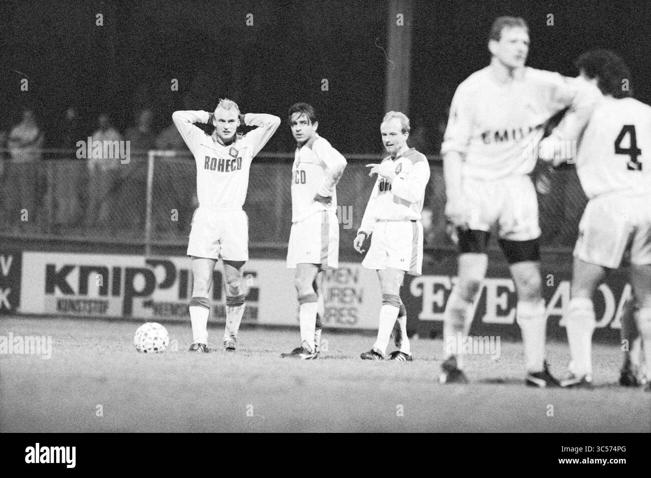 Telstar - Heracles, 15-03-1991 Whizgle News, Dutch Desk, Niederlande, 1950-2000 Eine Gruppe von vier Fußballspielern steht auf dem Spielfeld und zeigt sichtbare Anzeichen von Enttäuschung und Frustration, wahrscheinlich nach einem schwierigen Moment im Spiel. Ihre Ausdrucksformen spiegeln eine Mischung aus Besorgnis und Nachsicht wider, wobei ein Spieler den Kopf hält, während die anderen zuschauen und scheinbar die Situation reflektieren. Die Kulisse umfasst eine schwache Menschenmenge und Werbebanner, die die Szene in Stadionatmosphäre setzen. Stockfoto