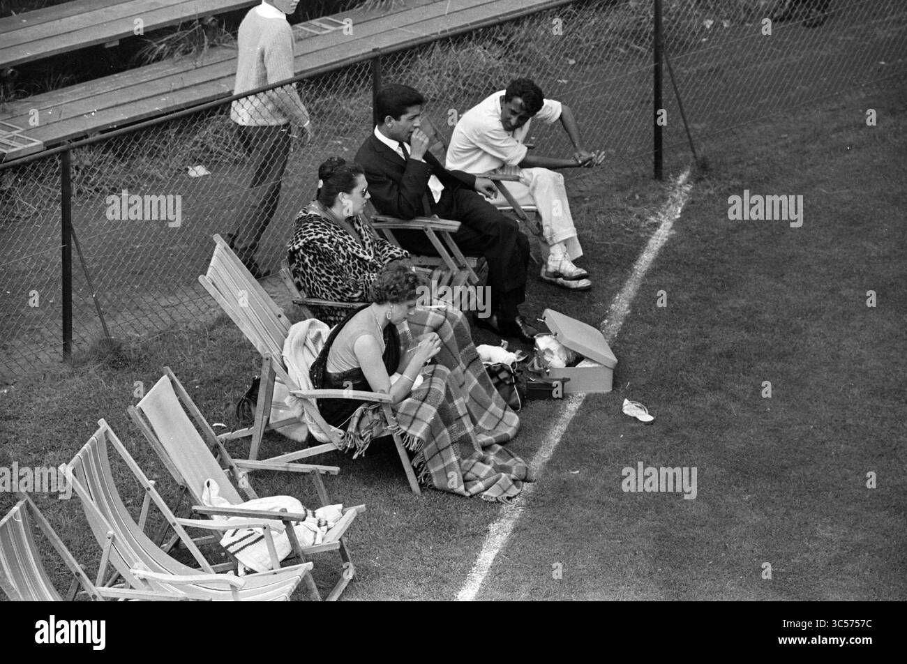 Niederlande - Indien, Cricket, 03-09-1961 Whizgle News, Dutch Desk, Niederlande, 1950-2000 Eine Gruppe von vier Personen sitzt auf Klappstühlen am Rande eines grasbewachsenen Feldes. Zwei Frauen, eine in einem gemusterten Schal und zwei Männer, eine in formeller Kleidung und die andere in eleganter Freizeitkleidung, unterhalten sich. In der Nähe liegt eine Box auf dem Boden, die auf ein Picknick oder eine Zusammenkunft hinweist. Die Umgebung wirkt entspannt und gesellig, mit leeren Stühlen um sie herum. Stockfoto