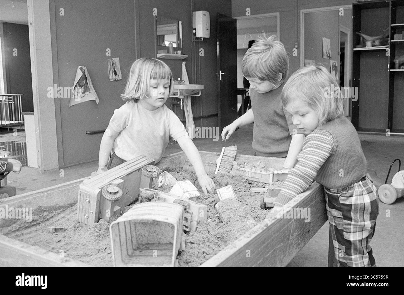 Alternative Spielgruppe, Schulen, 11-04-1973 Whizgle News, Dutch Desk, Niederlande, 1950-2000 drei Kinder spielen spielerisch an einem Sandtisch mit Spielzeugwagen und Werkzeugen. Ihre Neugier und Teamarbeit sind offensichtlich, während sie den Sand graben und erkunden, umgeben von einer gemütlichen Innenumgebung. Stockfoto