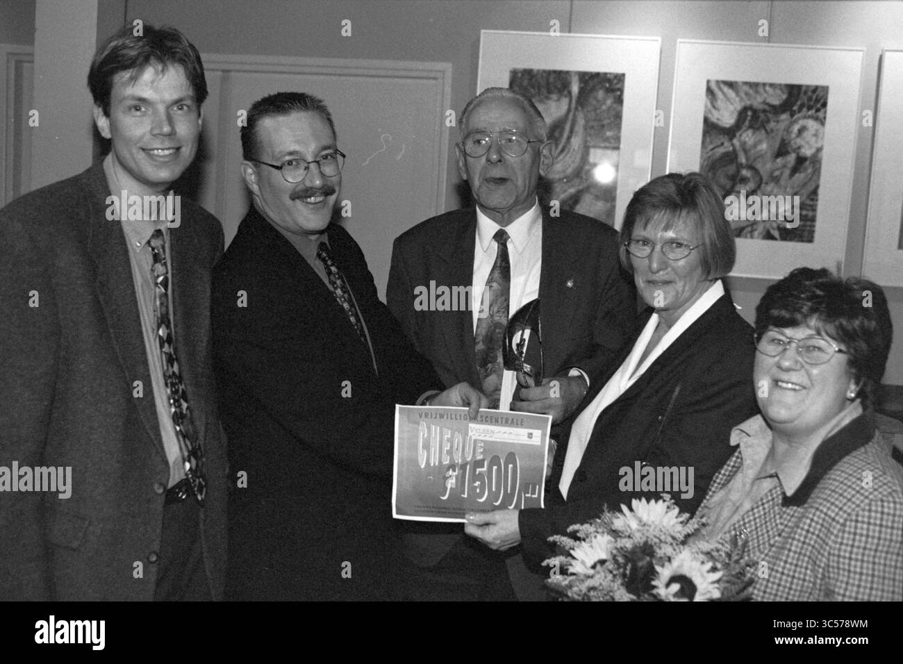 Volunteer Award 1997, IJmuiden, IJmuiden, Niederlande, 06-12-1997 Whizgle News, Dutch Desk, Niederlande, 1950-2000 Eine Gruppe von fünf Personen steht zusammen, lächelt und feiert eine Leistung. Eine Person besitzt eine Trophäe, während eine andere einen großen Scheck anzeigt, der eine Geldprämie anzeigt. Die Atmosphäre ist festlich, mit Kunstwerken im Hintergrund, die auf eine formelle Veranstaltung oder eine Anerkennungszeremonie hinweisen. Stockfoto