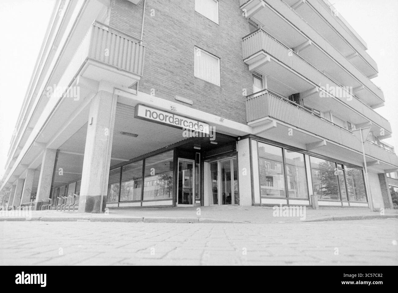 North Arcade Shopping Arcade, Geschäfte und Kioske, 09-08-1989 Whizgle News, Dutch Desk, Niederlande, 1950-2000 Ein modernes mehrstöckiges Gebäude verfügt über eine einladende Ladenfront mit der Bezeichnung „Noordarcade“. Die Architektur zeigt geometrische Linien und Balkondesigns, umgeben von einem geräumigen Bürgersteig. Leere Stühle säumen das Äußere und deuten auf eine ruhige Atmosphäre hin. Stockfoto