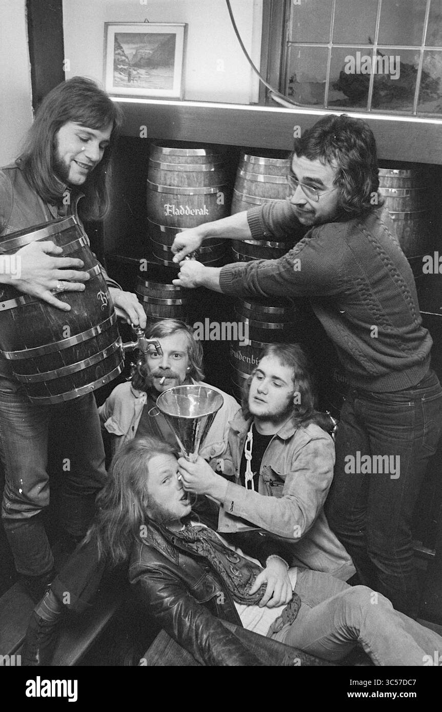Group Mushroom, Music, 07-12-1970 Whizgle News, Dutch Desk, Niederlande, 1950-2000 Eine Gruppe von fünf Männern feiert gemeinsam, wobei einer aus einem großen Fass strömt, während der andere eine Trophäe hält. Sie sind von Holzfässern umgeben und scheinen einen festlichen Moment zu genießen. Die Atmosphäre deutet auf Kameradschaft und ein Gefühl der Leistung hin. Stockfoto