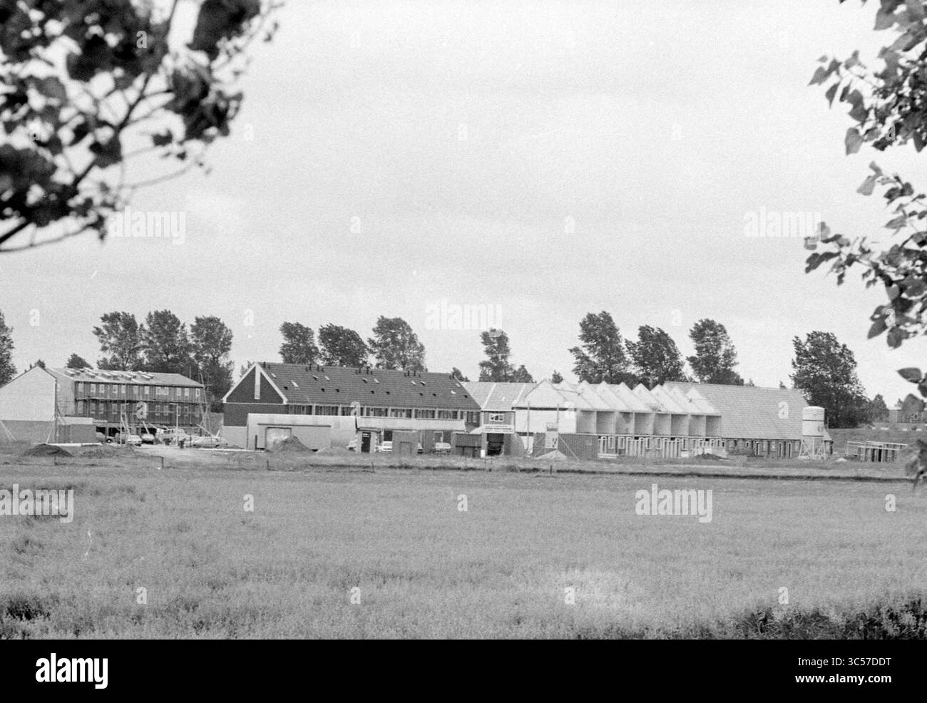 Bau von Solarenergiehäusern, Hoofddorp, Niederlande, 15-07-1984 Whizgle News, Dutch Desk, Niederlande, 1950-2000 Ein sich entwickelndes Viertel mit einer Mischung aus Wohngebäuden und Baustellen, umgeben von offenen Feldern und gesäumt von Bäumen, die sanft im Wind schweben. Stockfoto