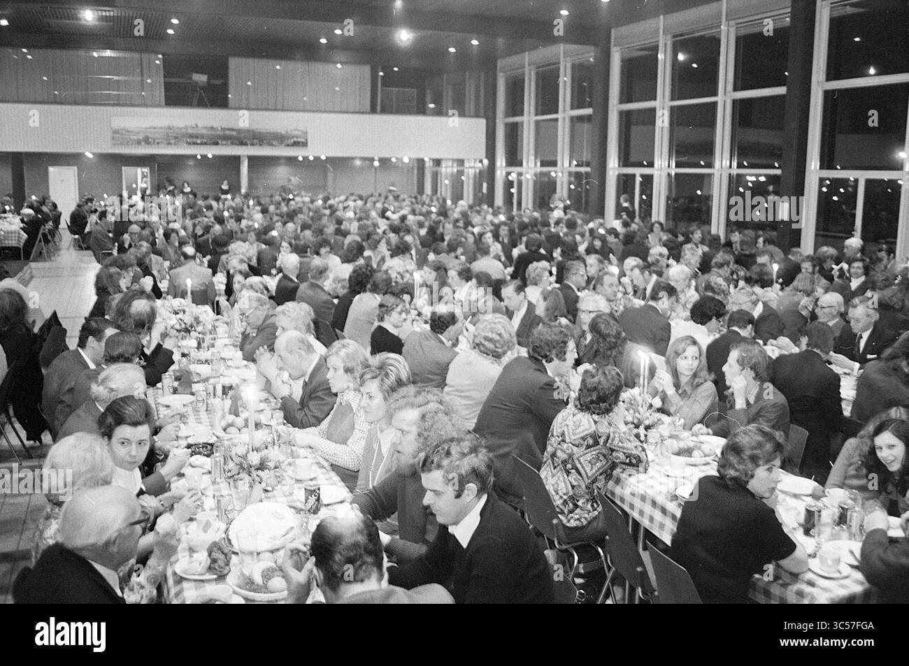 Chowder Meal, Hochofen-Schachturnier, 02-02-1974 Whizgle News, Dutch Desk, Niederlande, 1950-2000 Eine große Versammlung von Menschen sitzt an elegant gestalteten Tischen und genießt gemeinsam ein festliches Essen. Die Atmosphäre ist lebhaft, mit vielen Gesprächen und Interaktionen, die in der schwachen Beleuchtung der geräumigen Halle stattfinden. Stockfoto