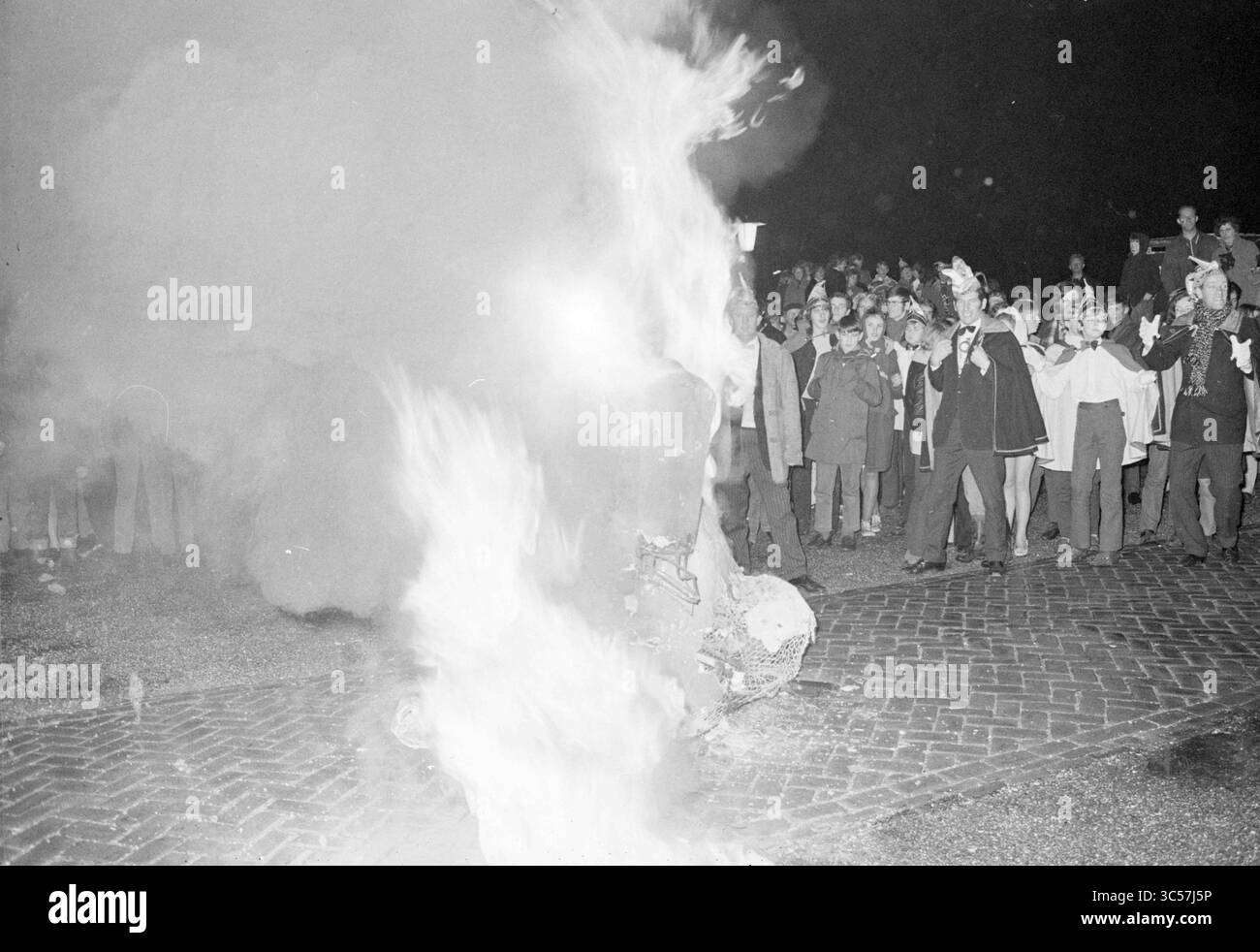 Burning Rabbit Noordwijkerhout, Karneval, 10-02-1970 Whizgle News, Dutch Desk, Niederlande, 1950-2000 Eine Menschenmenge versammelt sich im Dunkeln, fasziniert von der feurigen Ausstellung, während Flammen aus einer zentralen Figur ausbrechen und Rauch in die Nachtluft schleudern. Die Zuschauer, eine Mischung aus Erwachsenen und Kindern, sehen aufmerksam zu, einige mit erhobenen Armen in Aufregung oder Scheinfeier. Stockfoto