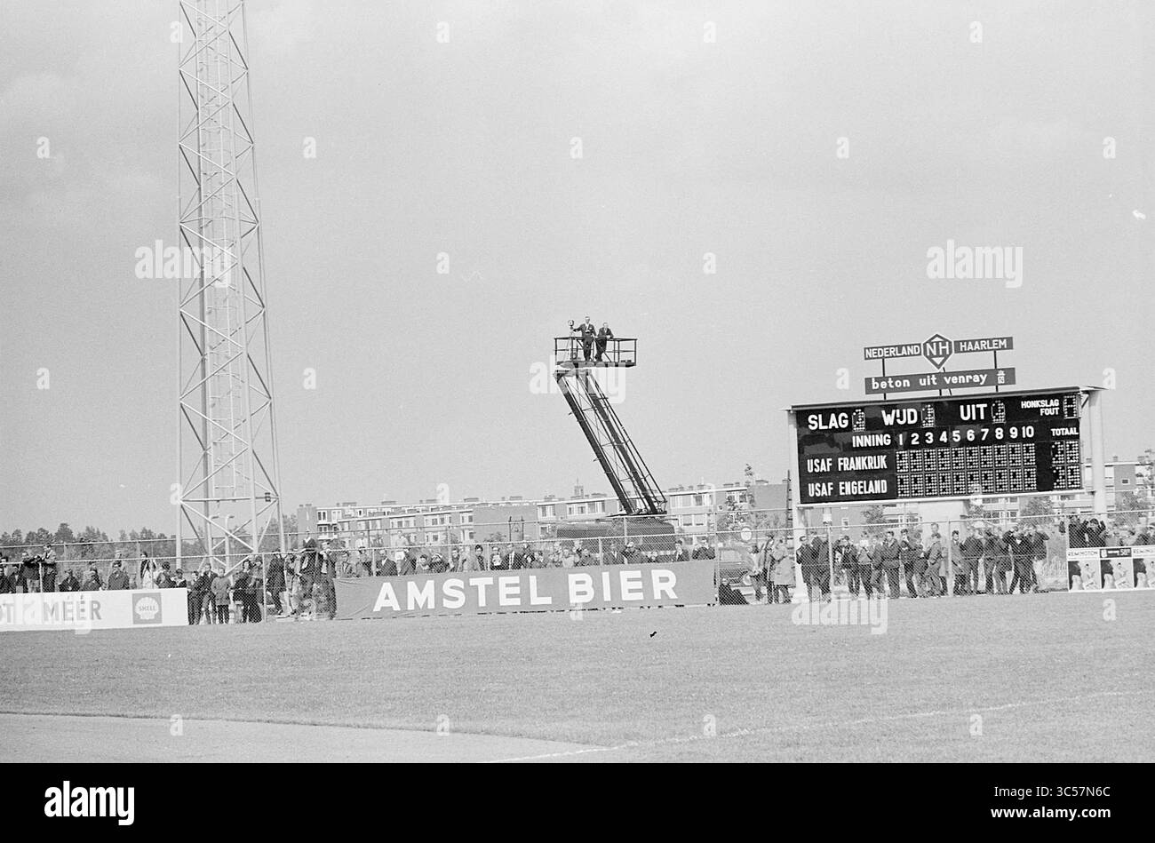 Haarlem Wird Geöffnet. Baseball Week and Film Match England France + Film II, Baseball, 29-07-1963 Whizgle News, Dutch Desk, Niederlande, 1950-2000 Eine belebte Sportstadionszene mit einer Anzeigetafel mit Spielstatistiken. Eine hohe Plattform mit mehreren Einzelpersonen fängt das Geschehen von oben ein, während sich die Zuschauer an der Seitenlinie versammeln. Werbebanner verbessern die Atmosphäre der Veranstaltung. Stockfoto