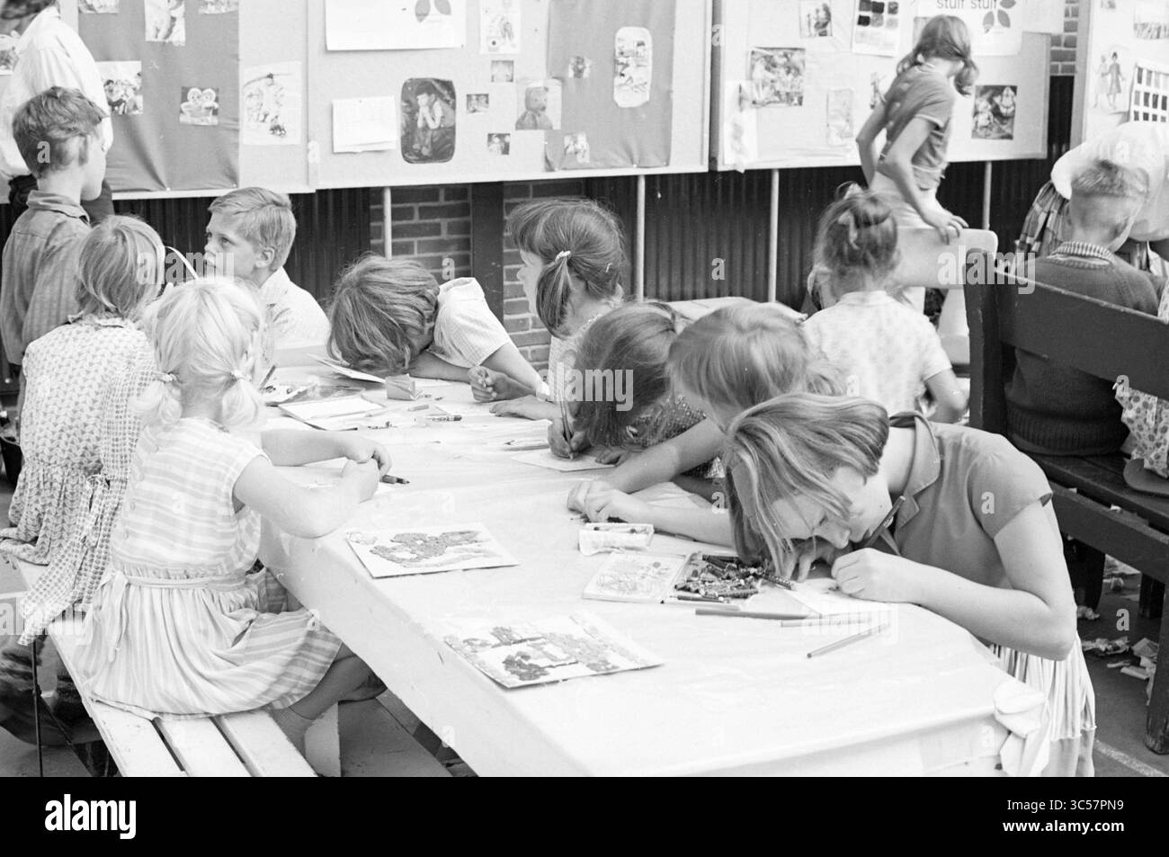 Aktivitäten Stuif Stuif, Stuif Stuif, 16-08-1965 Whizgle News, Dutch Desk, Niederlande, 1950-2000 Eine Gruppe von Kindern ist an einem großen Tisch an einer Kunstaktion beteiligt, die sich intensiv auf ihre Projekte konzentriert. Einige zeichnen oder färben, während andere sehr konzentriert zu sein scheinen und ihre Köpfe über ihre Arbeit gebeugt sind. Die lebendigen Dekorationen und Kunstwerke an den Wänden zeigen ihre Kreativität und Begeisterung. Stockfoto