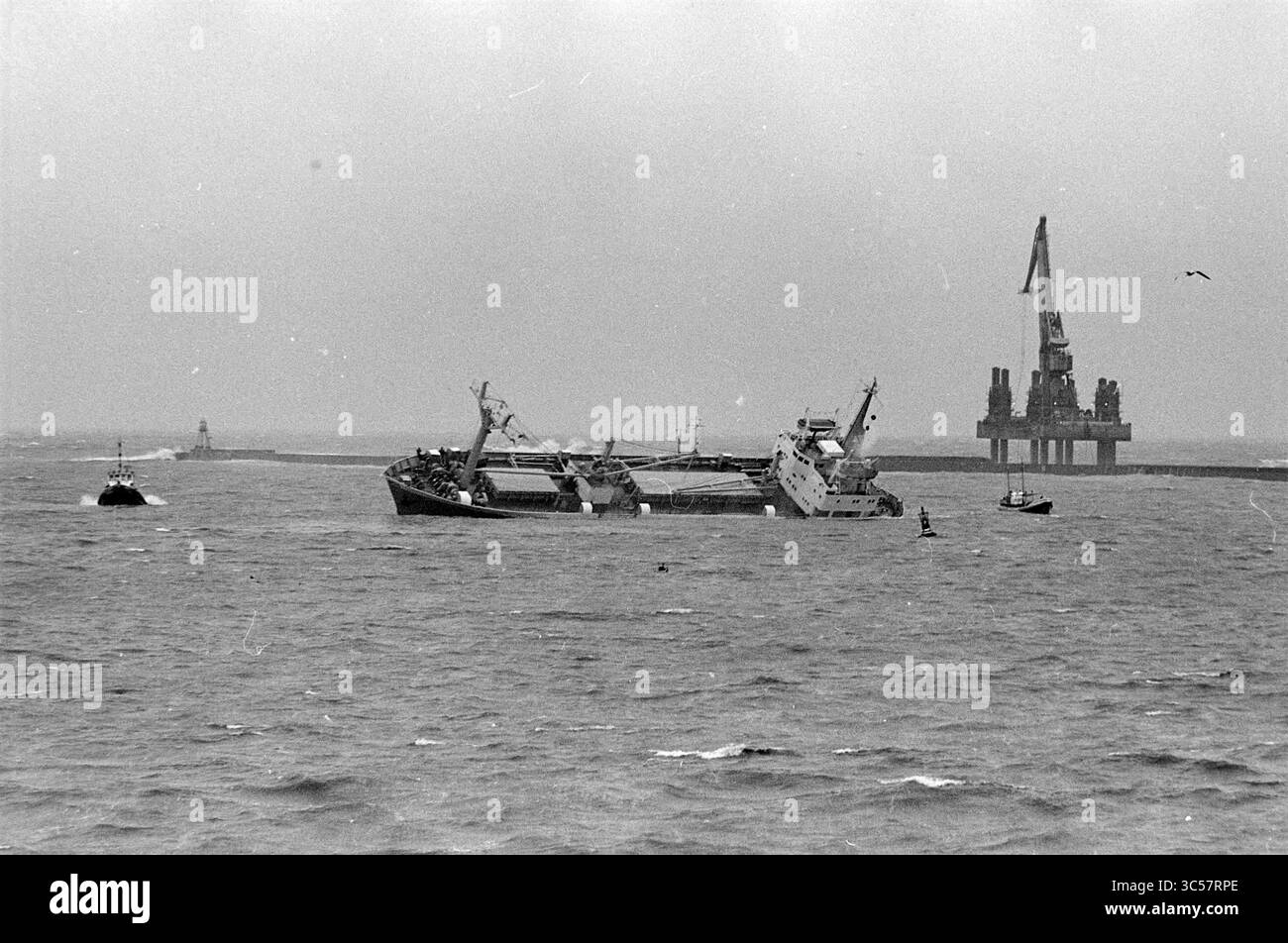 Der norwegische Frachter "Bretagne" führt wegen eines Lecks auf und ist geerdet, aber kentert weiter, IJmuiden, Bergingshaven, Niederlande, 28-03-1966 Whizgle News, Dutch Desk, Niederlande, 1950-2000 Ein in Schwierigkeiten geratenes Schiff tauchte teilweise in turbulenten Gewässern unter, mit einer entfernten Ölplattform und kleineren Schiffen, die in der Nähe unter einem trüben, bedeckten Himmel navigieren. Stockfoto