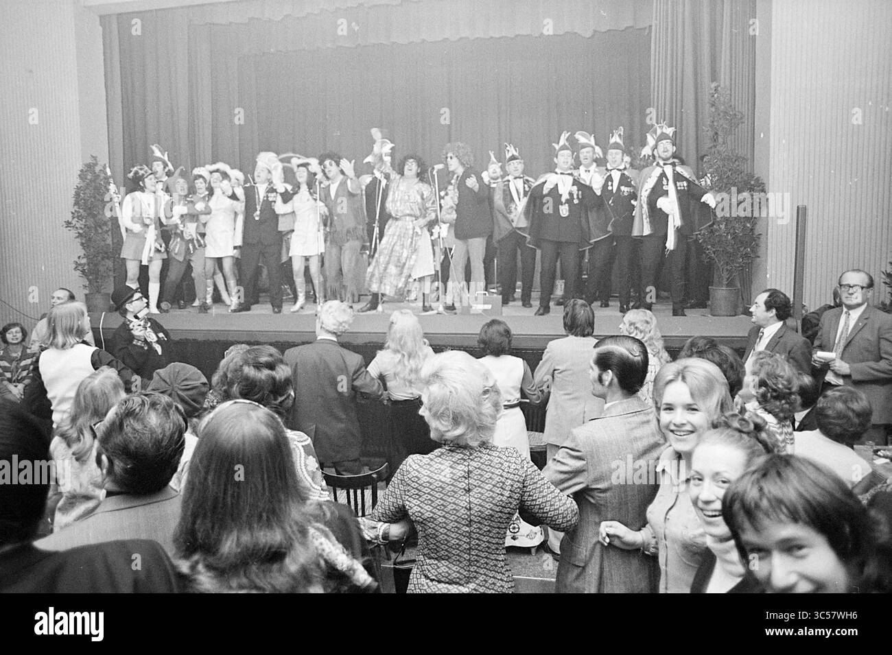 Buntes abendliches Blast Furnace Chess Tournament, Blast Furnace Chess Tournament, 27-01-1972 Whizgle News, Dutch Desk, Niederlande, 1950-2000 Eine lebhafte Bühnenvorstellung mit einer vielfältigen Gruppe von Entertainern in Kostümen, die sich freudig mit einem begeisterten Publikum beschäftigen. Die Szene fängt eine festliche Atmosphäre ein, in der die Menschen lächeln und feiern, was ein Gefühl der Gemeinschaft und Spannung schafft. Stockfoto