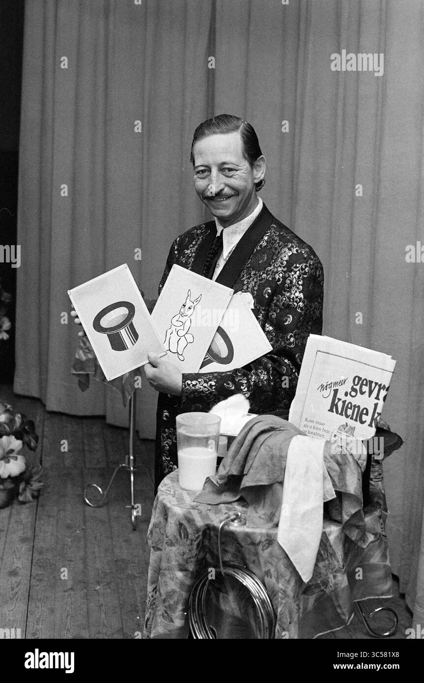 Daan Vrolijk, Magician, Report, 04.09.1972 Whizgle News, Dutch Desk, Niederlande, 1950-2000 Ein fröhlicher Zauberer in dekorativem Outfit hält illustrierte Karten mit einem Hut und einem Kaninchen hoch, während er neben einem Tisch steht, der mit verschiedenen Requisiten und Tüchern geschmückt ist. Der Hintergrund lässt eine Bühnensituation vermuten, die das Thema Performance und Illusion unterstreicht. Stockfoto