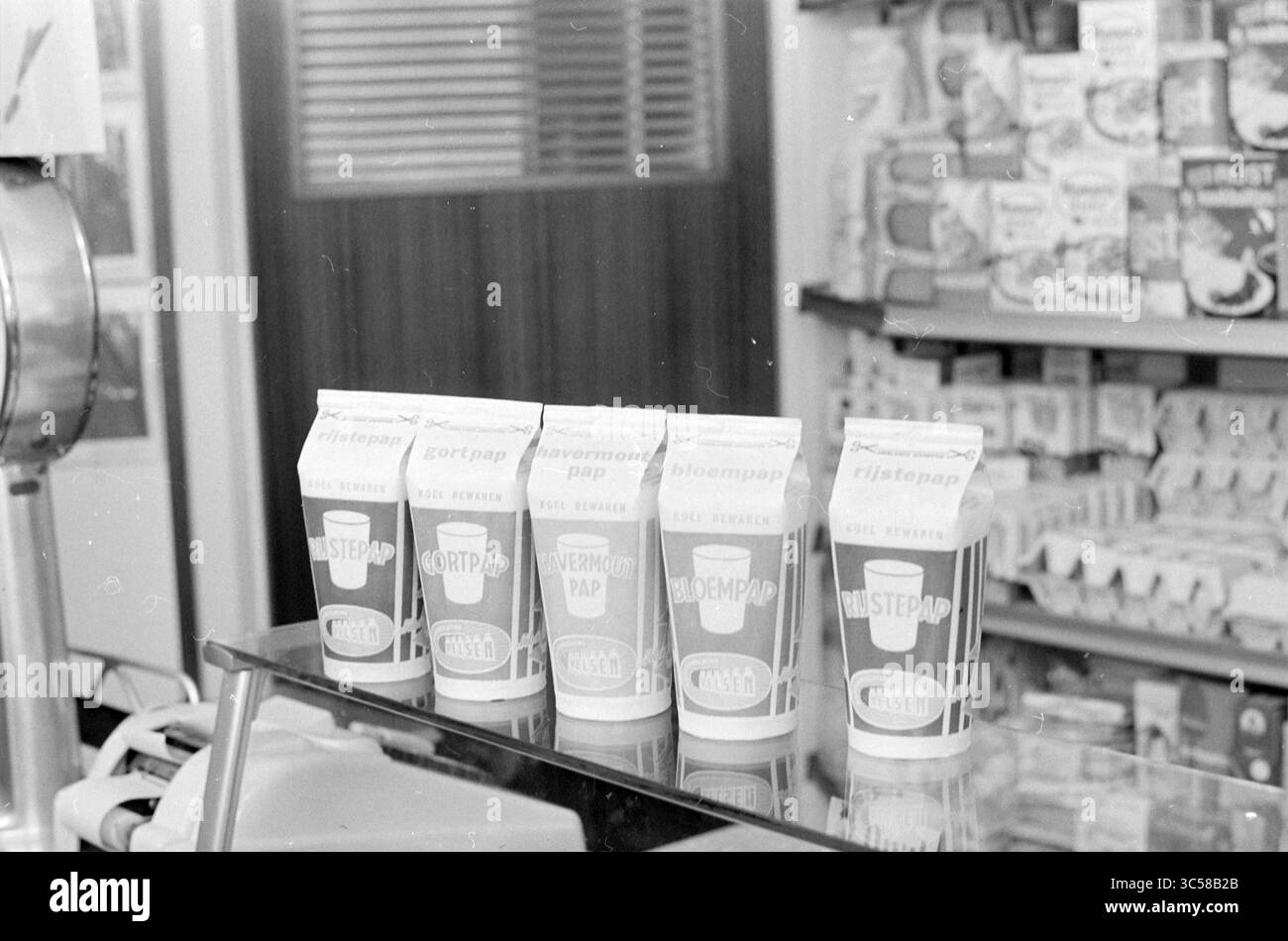 Neue Milchkartons, dekorative Kanne, Milch, Milchhändler, Milchmänner, 23-06-1966 Whizgle News, Dutch Desk, Niederlande, 1950-2000 Eine Ausstellung von Vintage-Milchkartons auf einer Arbeitsplatte, die verschiedene Geschmacksrichtungen mit einfachen, auffälligen Grafiken präsentiert. Dahinter sorgen Regale mit verpackten Waren für eine nostalgische Lebensmittellandatmosphäre. Stockfoto