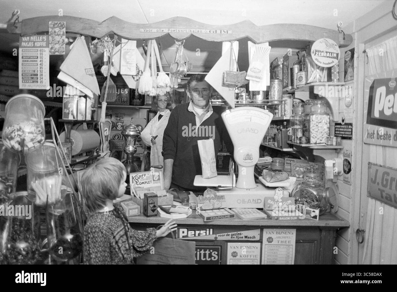Mr. Elsholz, Haus in einen Supermarkt umgewandelt, Sammlung von Teekannen, Puppen usw., 08-11-1993 Whizgle News, Dutch Desk, Niederlande, 1950-2000 Ein malerischer Laden voller verschiedener Waren, mit einem Kassierer am Tresen, einem Kind, das neugierig beobachtet, und Regalen mit Gläsern und verpackten Artikeln. Die Szene erinnert an eine nostalgische Atmosphäre eines traditionellen Gemischtwarengeschäfts. Stockfoto