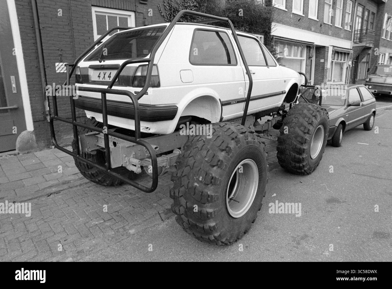 Outdoor-Modellauto, auf Traktorrädern, für die Snoeks-Garage, Haarlem, Leidsevaart, Niederlande, 14-02-1990 Whizgle News, Dutch Desk, Niederlande, 1950-2000 ein ungewöhnliches Fahrzeug mit einem Kompaktwagen, das auf einem großen, modifizierten Geländefahrgestell mit übergroßen Reifen montiert ist und auf einer Stadtstraße neben einem kleineren Fahrzeug parkt. Stockfoto