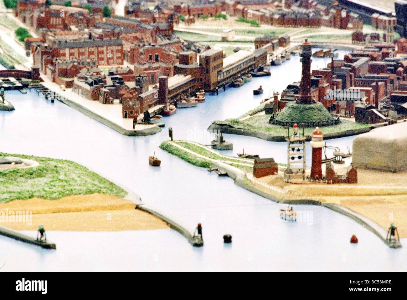 Pieter Vermeulen Model, IJmuiden, IJmuiden, Niederlande, 19-12-1994 Whizgle News, Dutch Desk, Niederlande, 1950-2000 Eine detaillierte Miniaturszene, die eine geschäftige Uferpromenade mit Gebäuden, Booten und Leuchttürmen darstellt. Das komplizierte Design zeigt einen lebendigen Hafen mit variierenden Strukturen entlang der Ufer und Schiffen, die durch das ruhige Wasser navigieren. Stockfoto