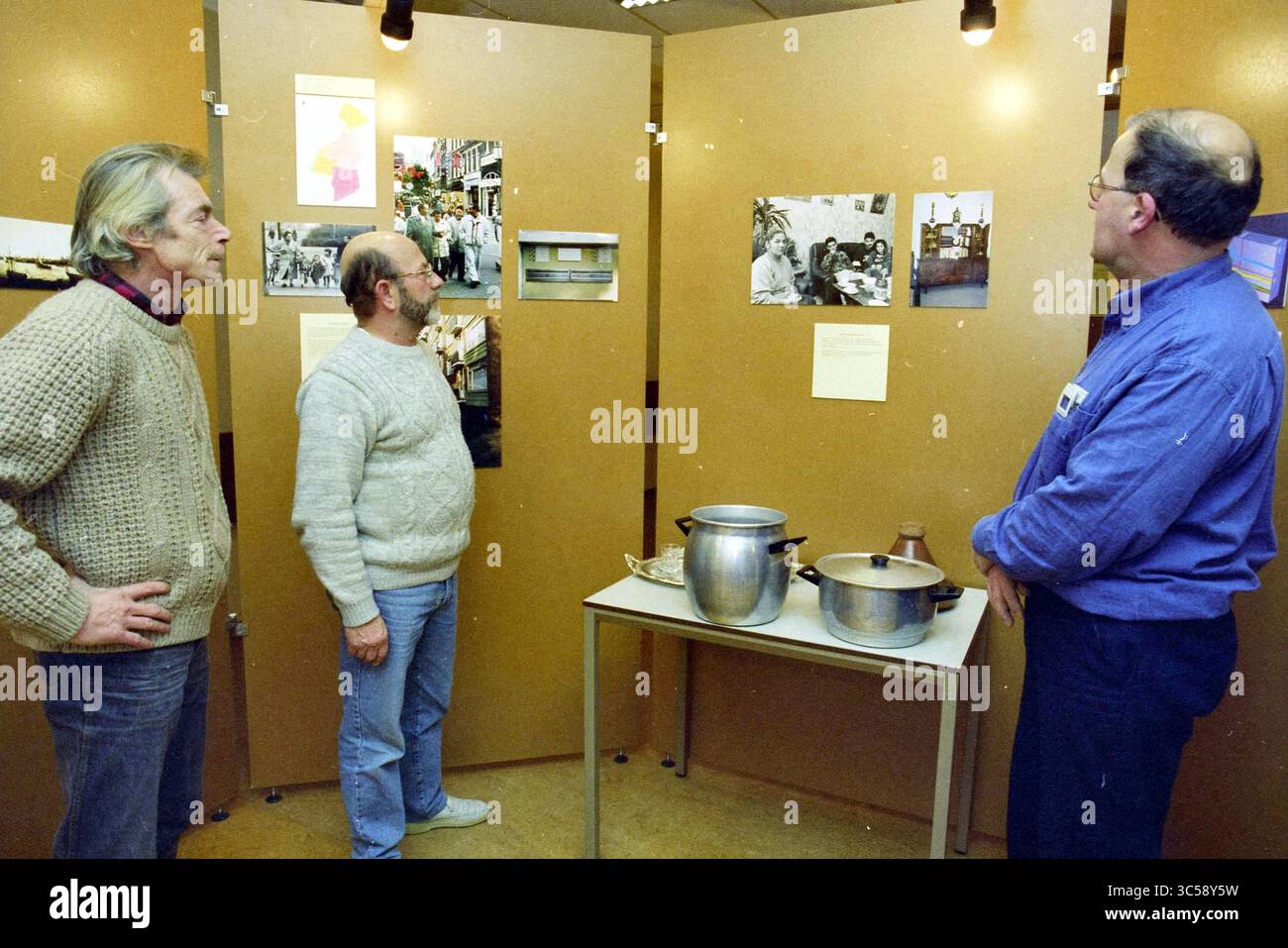 Ausstellung im Spaarne, H'lem, Haarlem, Niederlande, 06-12-1995 Whizgle News, Dutch Desk, Niederlande, 1950-2000 drei Personen diskutieren, während sie eine Reihe von Displays mit Fotos und informativen Tafeln beobachten. Sie untersuchen historische Bilder und Artefakte, einschließlich Kochtöpfe, während sie Einblicke in die Ausstellungen geben. Die Umgebung scheint ein Gemeinschafts- oder Bildungsraum zu sein, der der lokalen Geschichte oder Kultur gewidmet ist. Stockfoto