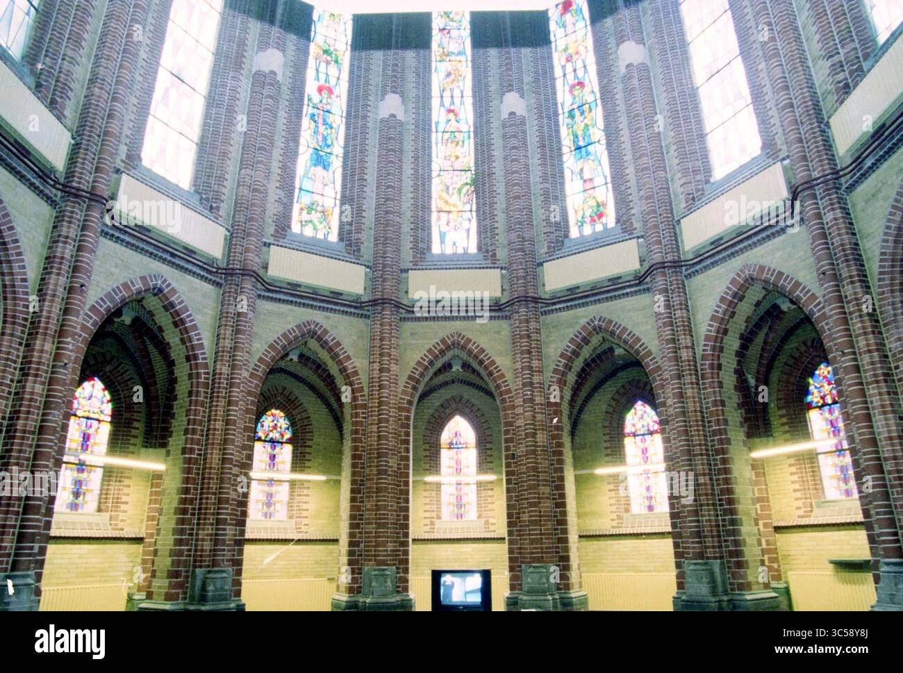 Sacred Heart Church, Apartments, Haarlem, Niederlande, 02-09-1998 Whizgle News, Dutch Desk, Niederlande, 1950-2000 Ein atemberaubender Innenraum mit hoch aufragenden Ziegelbögen und hohen, bunten Buntglasfenstern, die den Raum mit komplexen Mustern und Licht beleuchten. Das architektonische Design betont Pracht und ein Gefühl der Ruhe. Stockfoto