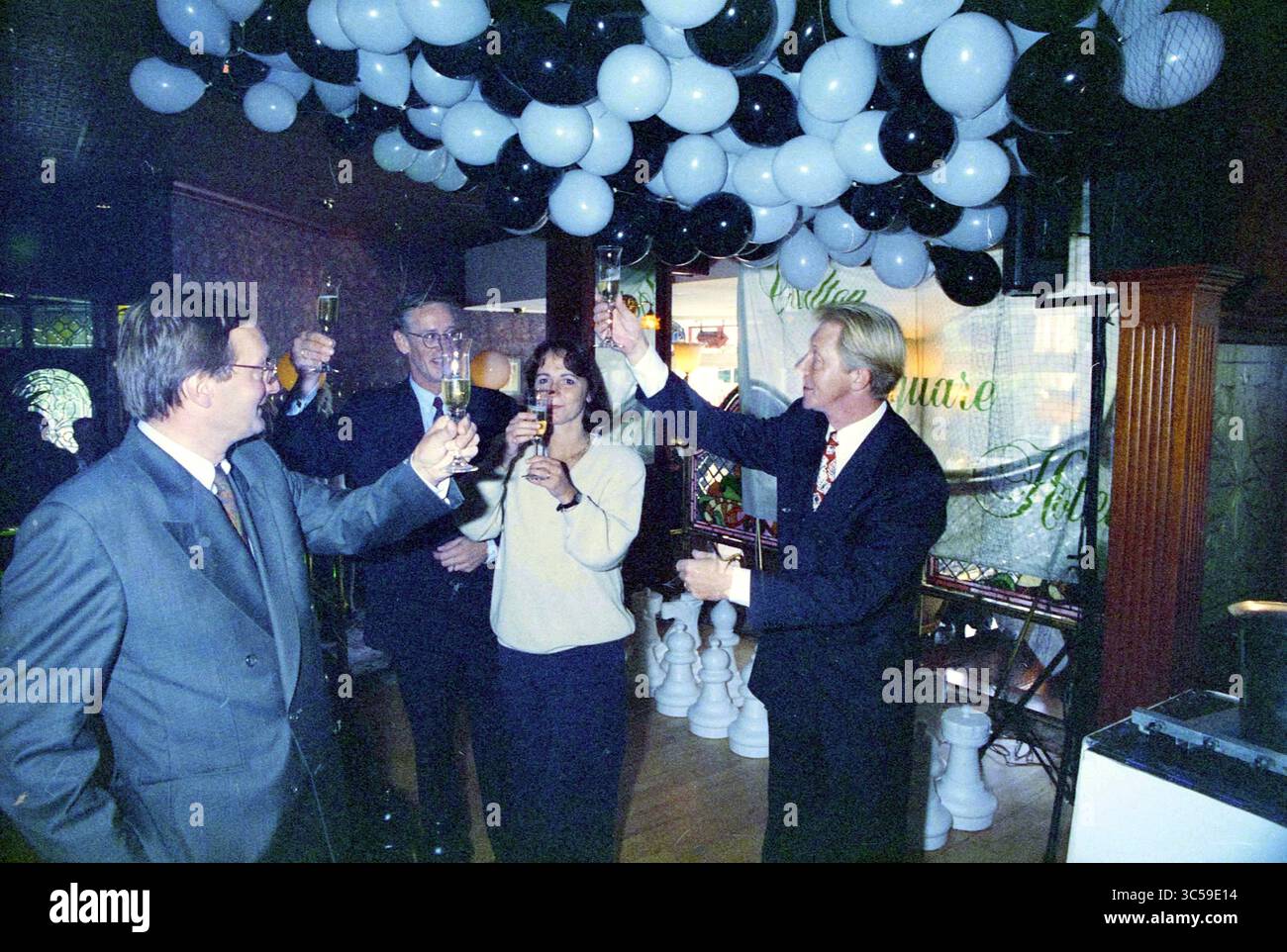 Inbetriebnahme des Schachspiels, 15-09-1994 Whizgle News, Dutch Desk, Niederlande, 1950-2000 Eine Gruppe elegant gekleideter Einzelpersonen hebt ihre Brille in einem feierlichen Toast unter einer auffälligen Anzeige von schwarz-weißen Ballons und schafft eine festliche Atmosphäre. Stockfoto