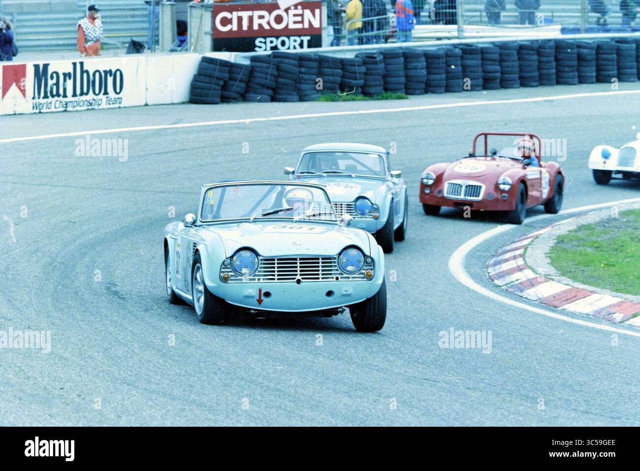 Historisches Autorennen, Zandvoort Circuit, Zandvoort, 10-05-1997 Whizgle News, Dutch Desk, die Niederlande, 1950-2000 klassische Rennwagen fahren auf einer kurvenreichen Strecke und zeigen ihr Vintage-Design und ihren Wettkampfgeist. Dem Hauptfahrzeug mit seinem markanten Kühlergrill folgen weitere Fahrzeuge, die jeweils eine andere Ära der Automobiltechnik repräsentieren. Spannung erfüllt die Luft, während sie in Richtung der kommenden Kurve rasen. Stockfoto